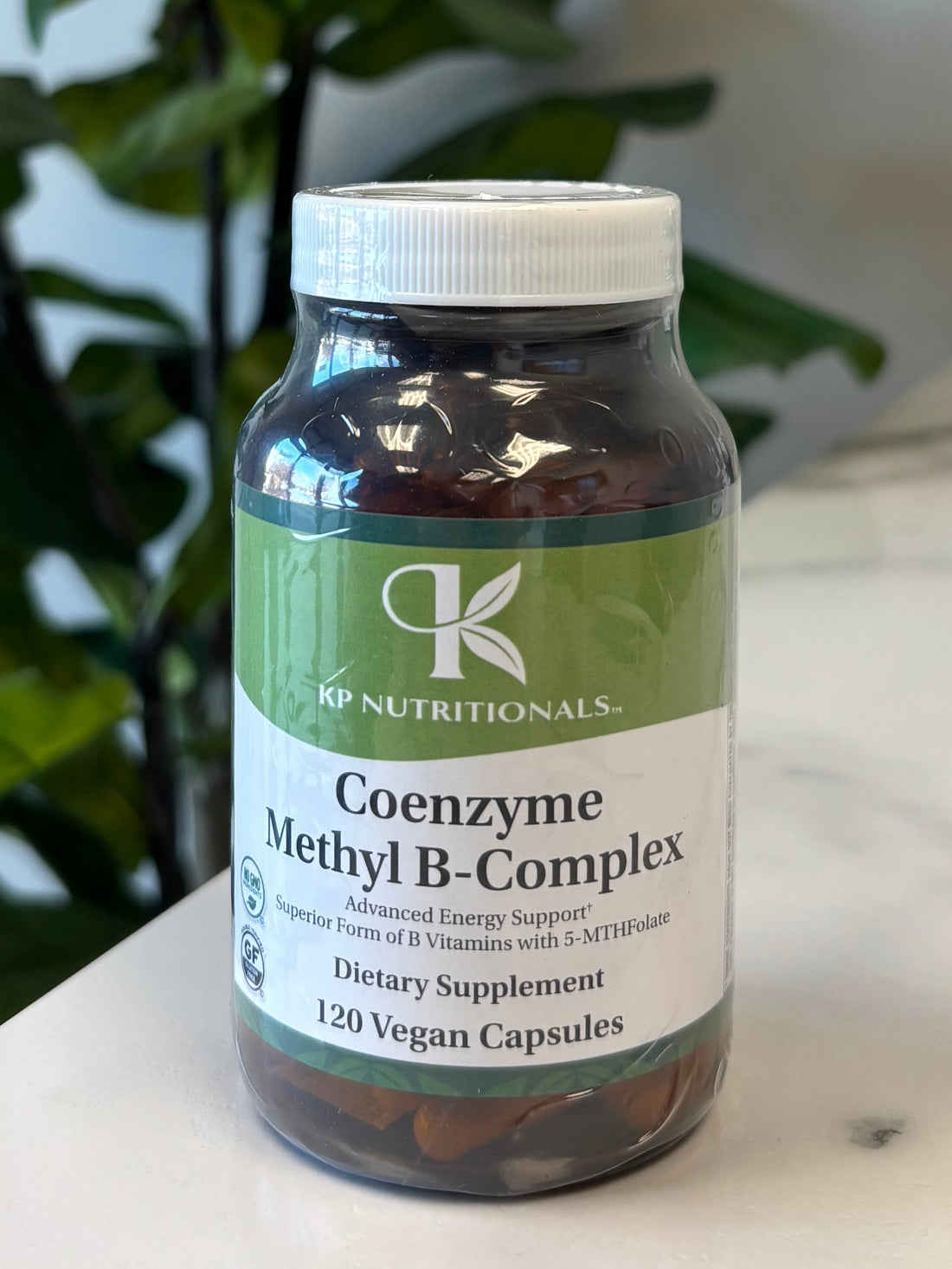 Bottle of Coenzyme Methyl B-Complex supplement on a marble surface with a plant in the foreground