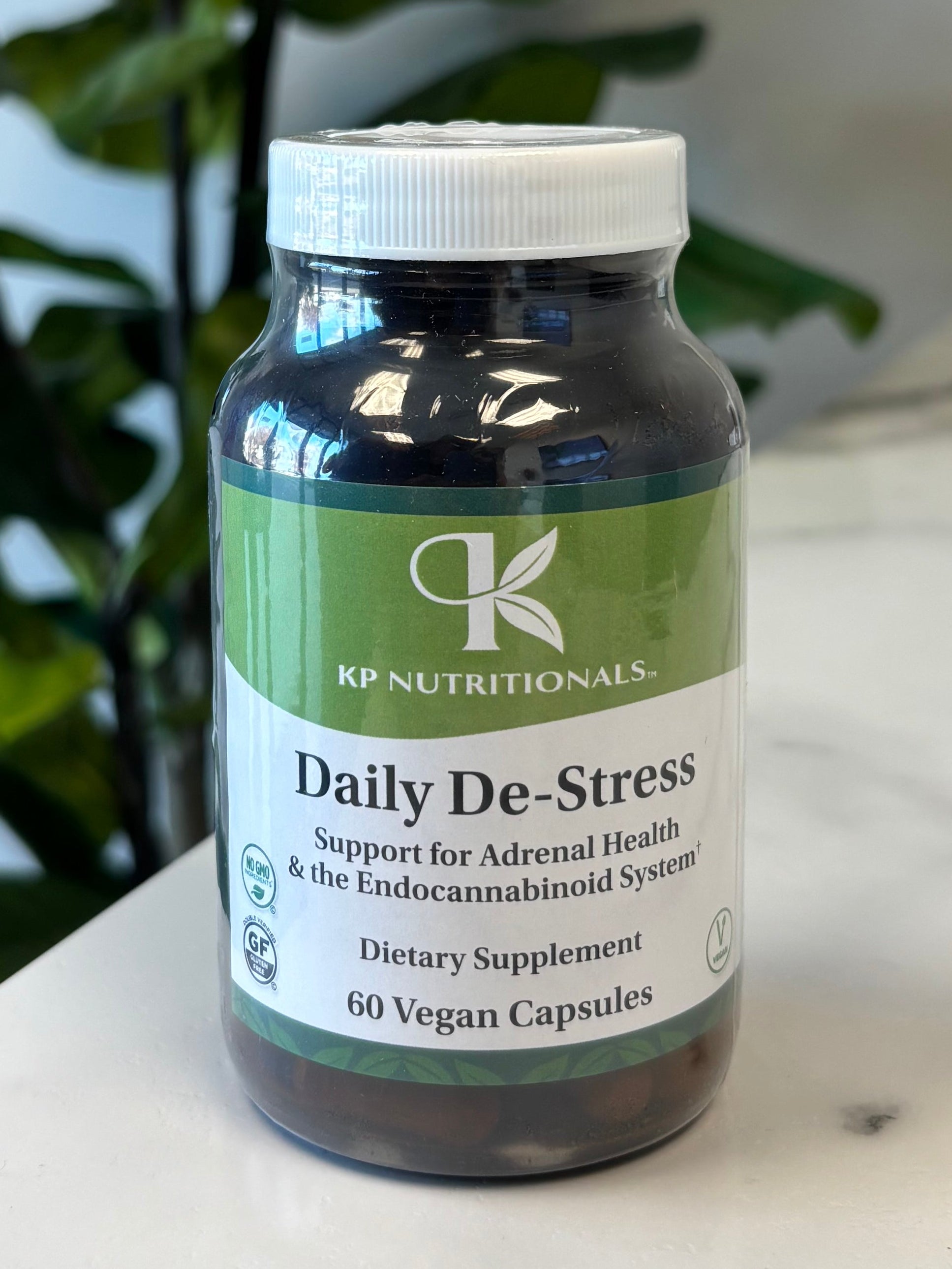 Bottle of Daily De-Stress supplement on a marble surface with green leaves in the foreground