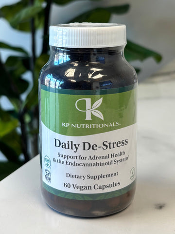 Bottle of Daily De-Stress supplement on a marble surface with green leaves in the foreground