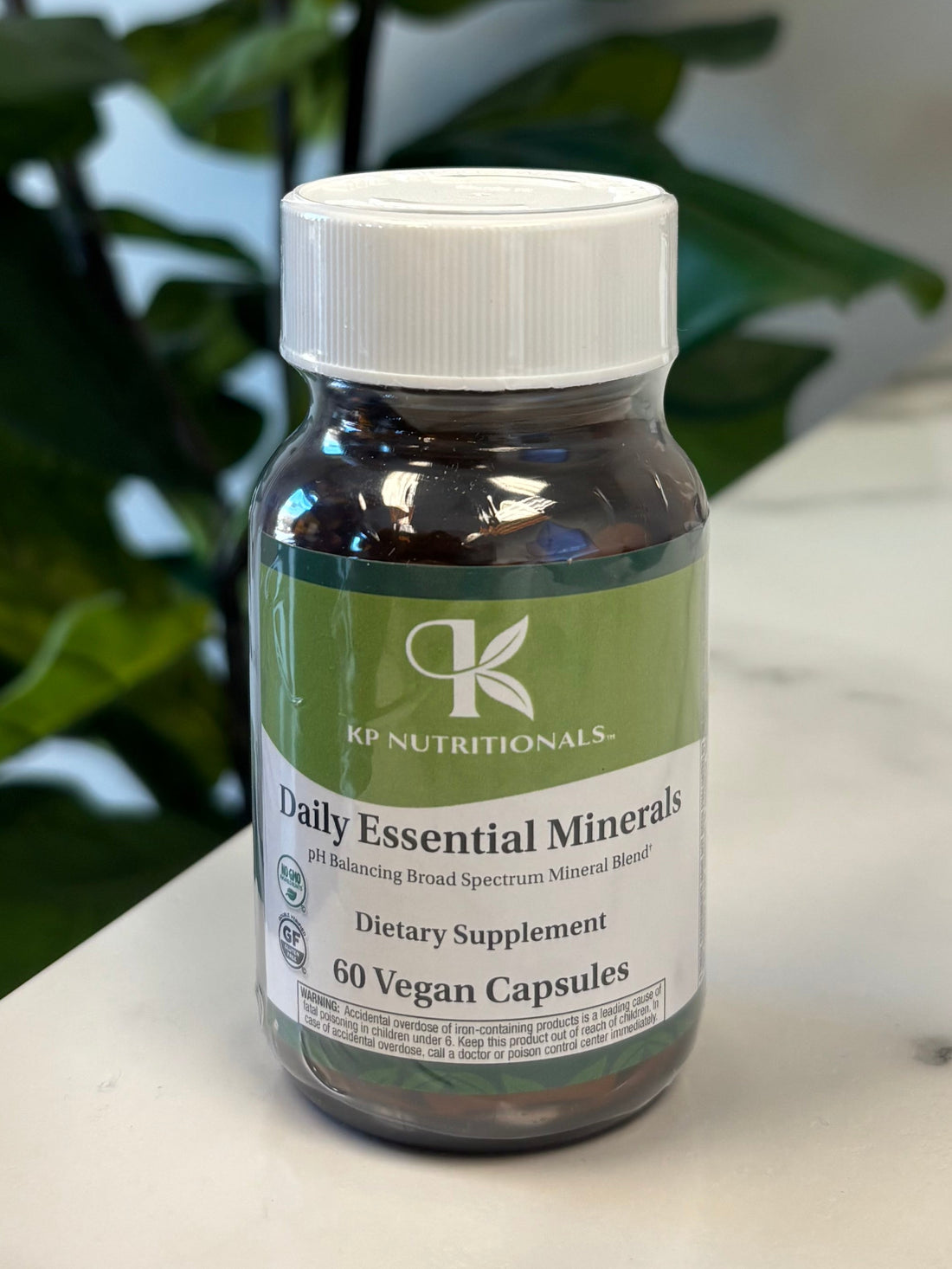 Bottle of Daily Essential Minerals with a plant in the foreground on a marble surface