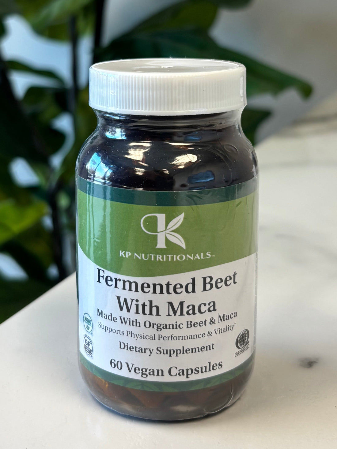 Supplement bottle Fermented Beet with Maca with green label on a marble surface with a plant in the foreground