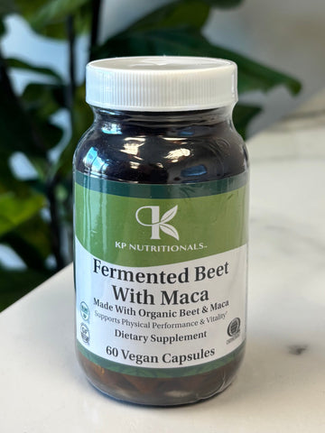 Supplement bottle Fermented Beet with Maca with green label on a marble surface with a plant in the foreground