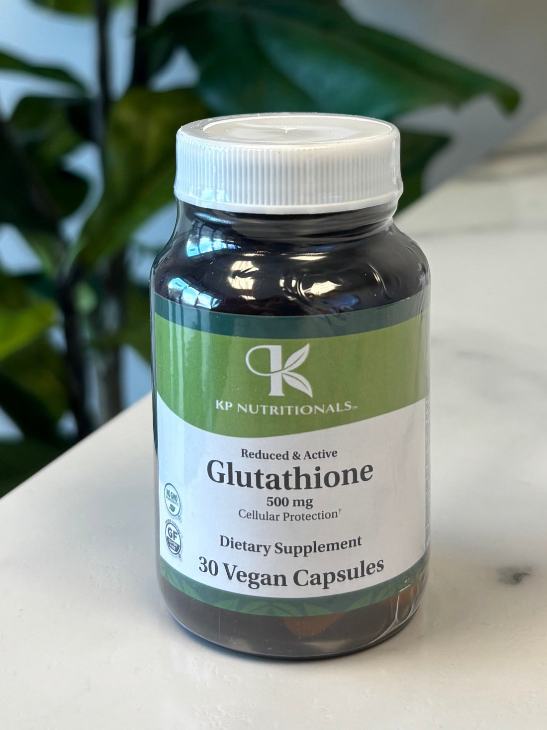 Bottle of Glutathione on a marble surface with a plant in the foreground