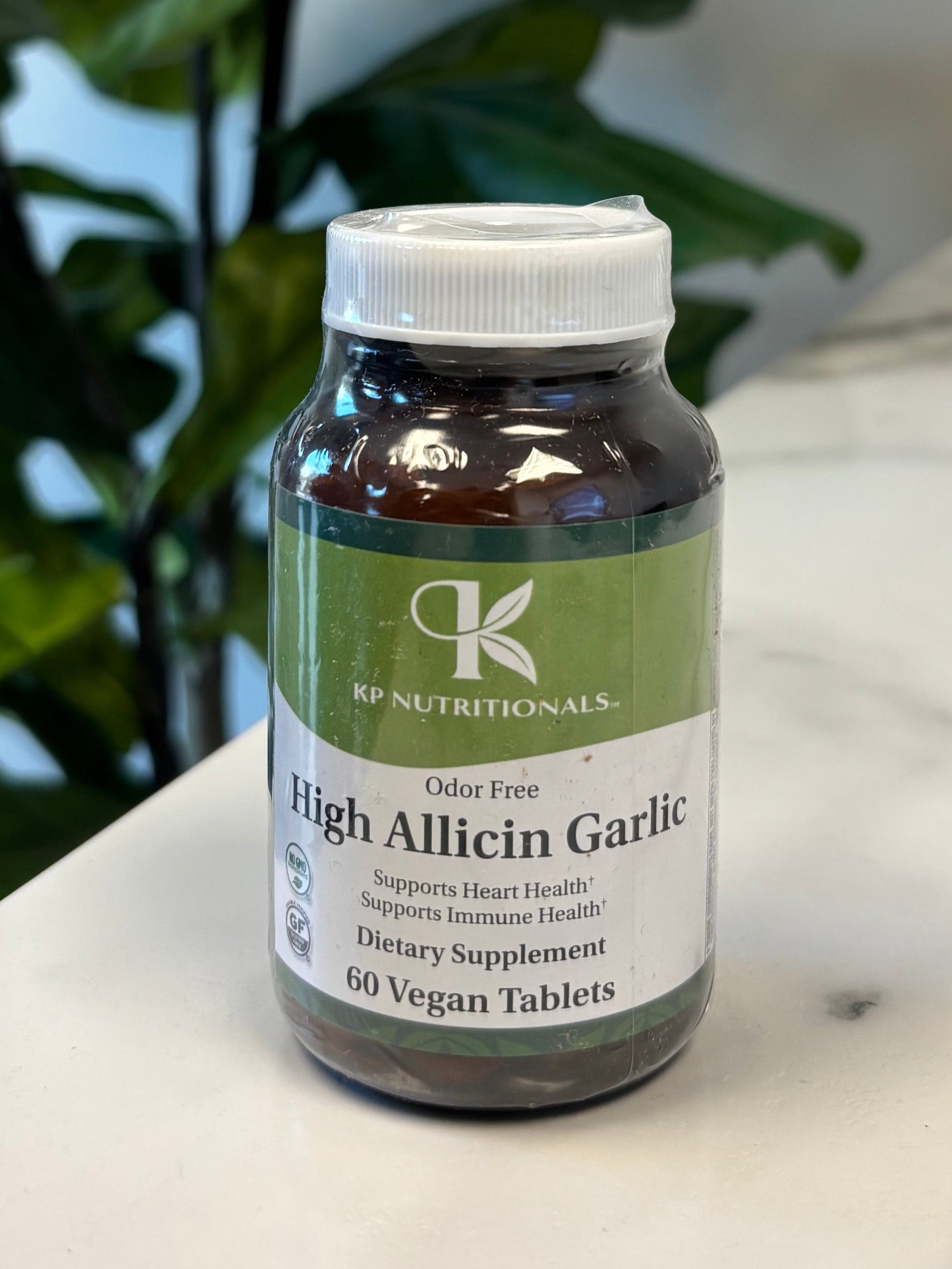 Bottle of High Allicin Garlic supplement on a Marble Surface with Green Leaves in foreground