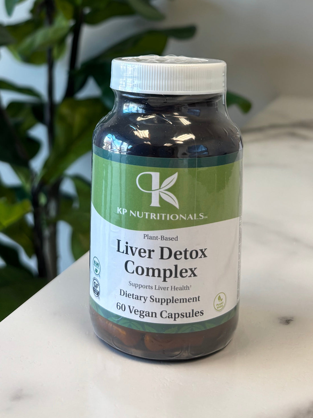 Supplement bottle labeled 'Liver Detox Complex' on a marble surface with a plant in the foreground