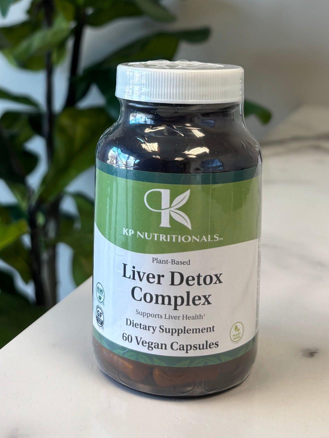 Supplement bottle labeled 'Liver Detox Complex' on a marble surface with a plant in the foreground