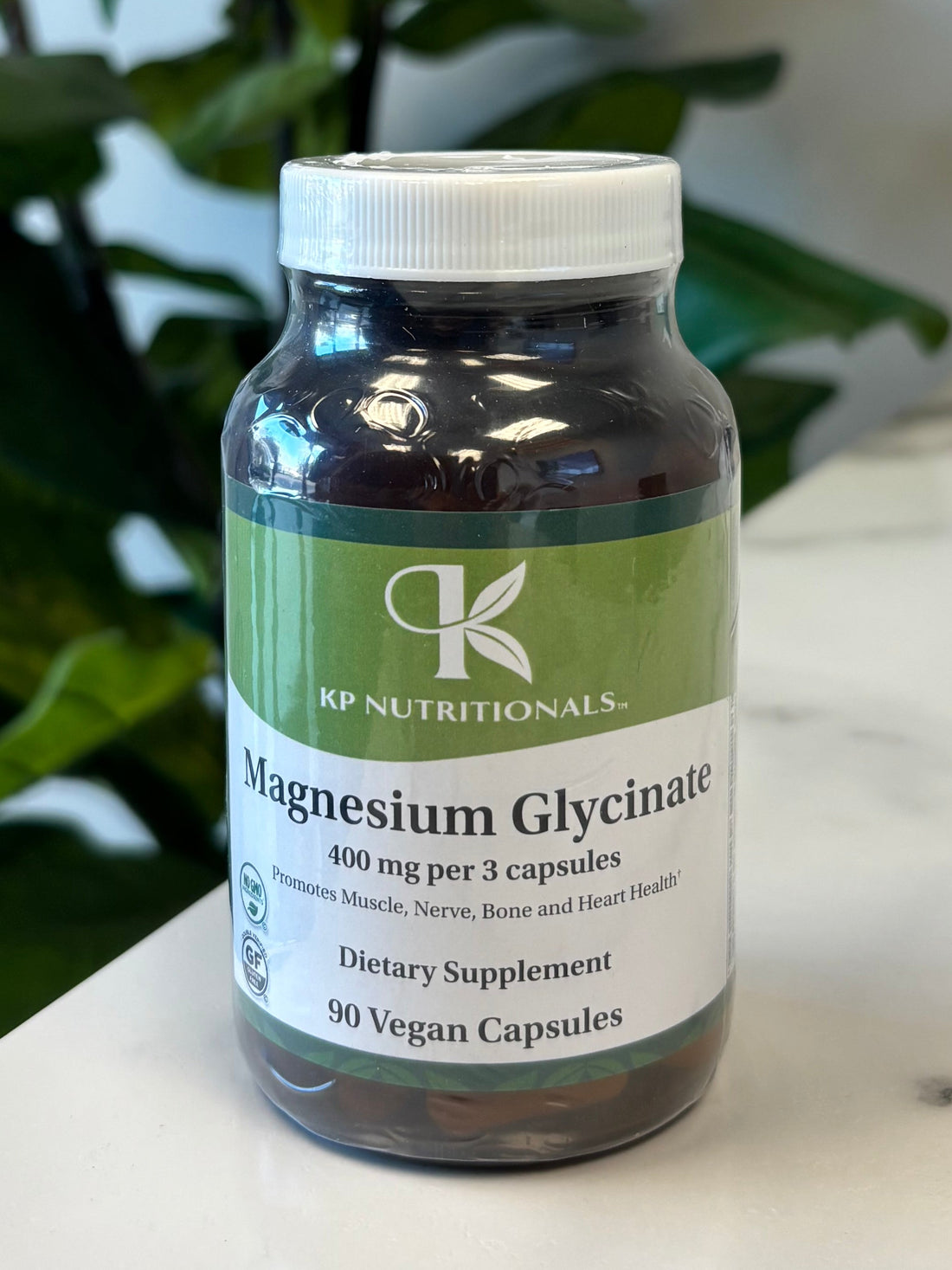 Bottle of magnesium glycinate supplement on a marble surface with green leaves in the background