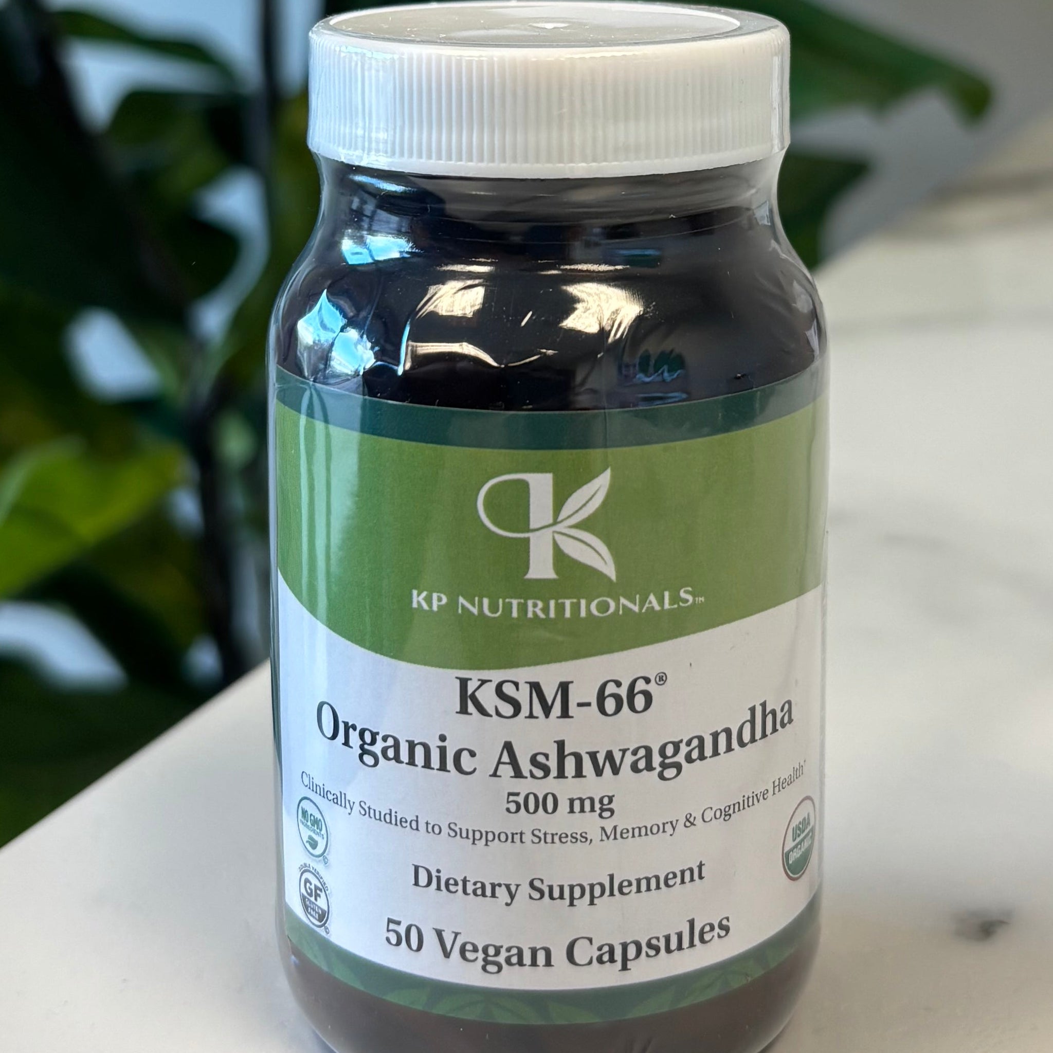 Supplement bottle Organic Ashwagandha on a marble surface with a plant in the foreground