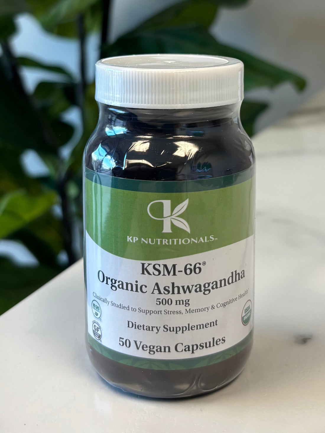 Supplement bottle Organic Ashwagandha on a marble surface with a plant in the foreground