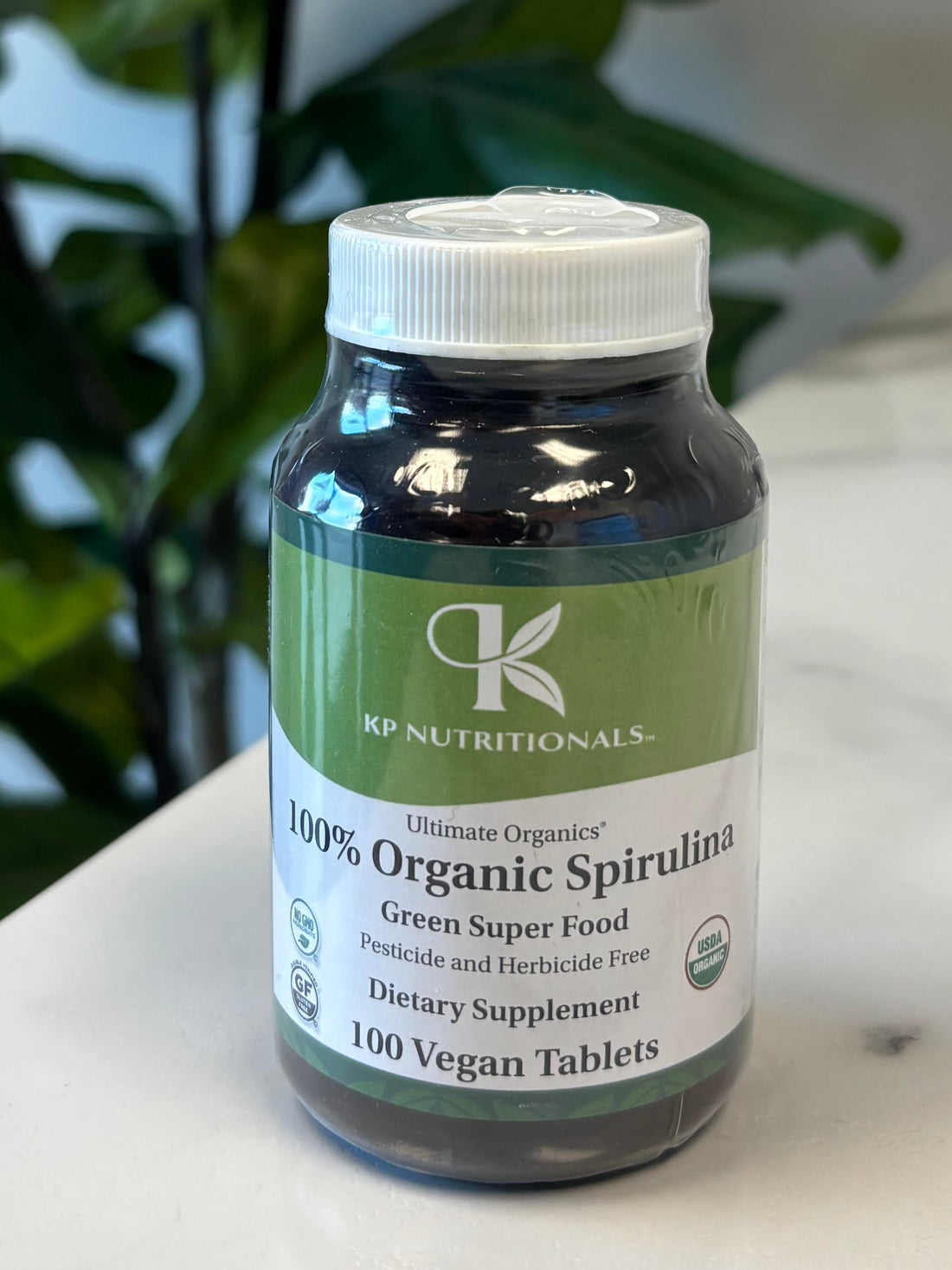 Bottle of organic spirulina on a marble surface with green leaves in the foreground