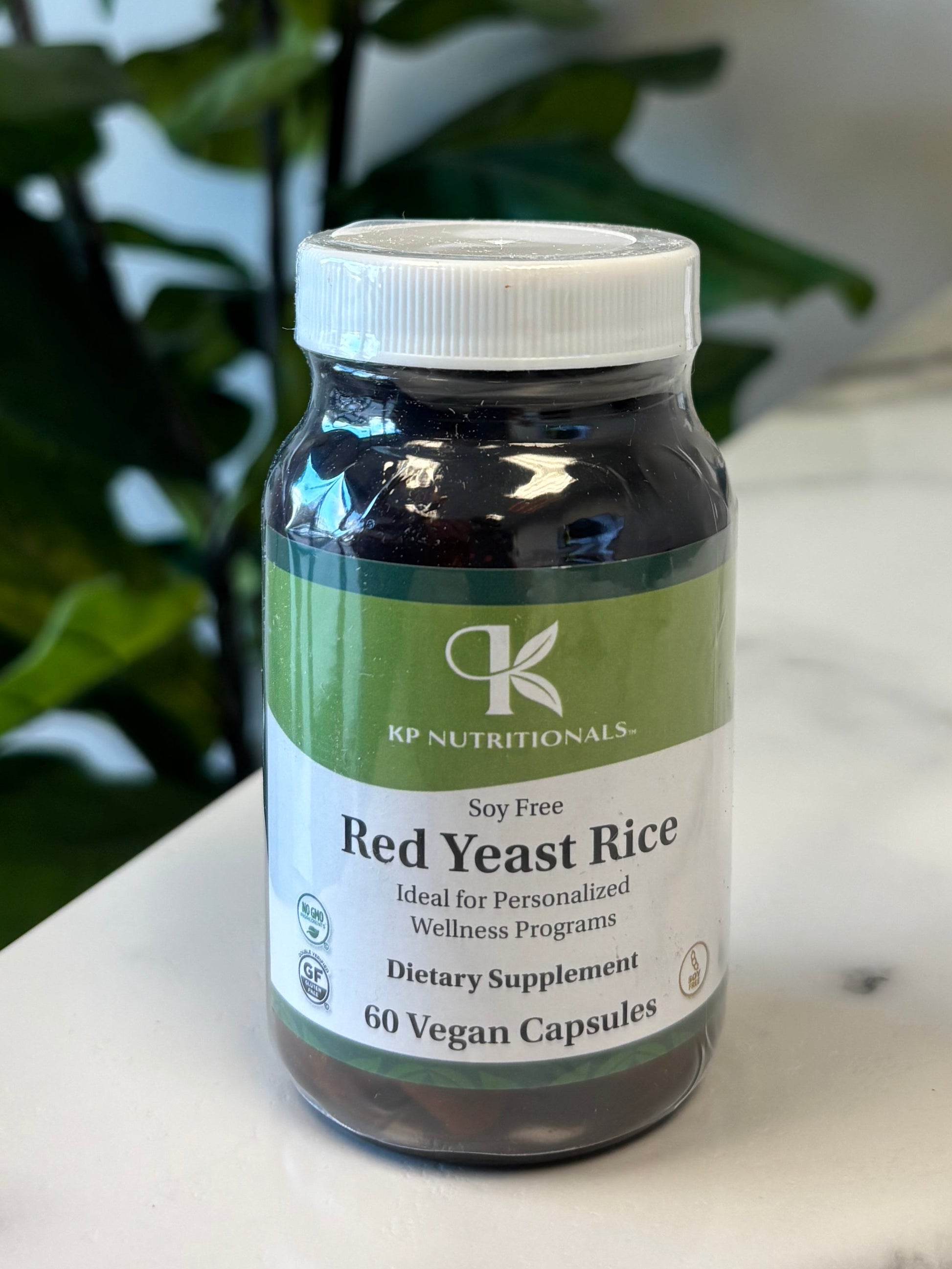 Bottle of Red Yeast Rice supplement on a marble surface with green leaves in the foreground