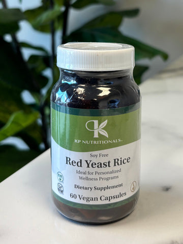 Bottle of Red Yeast Rice supplement on a marble surface with green leaves in the foreground