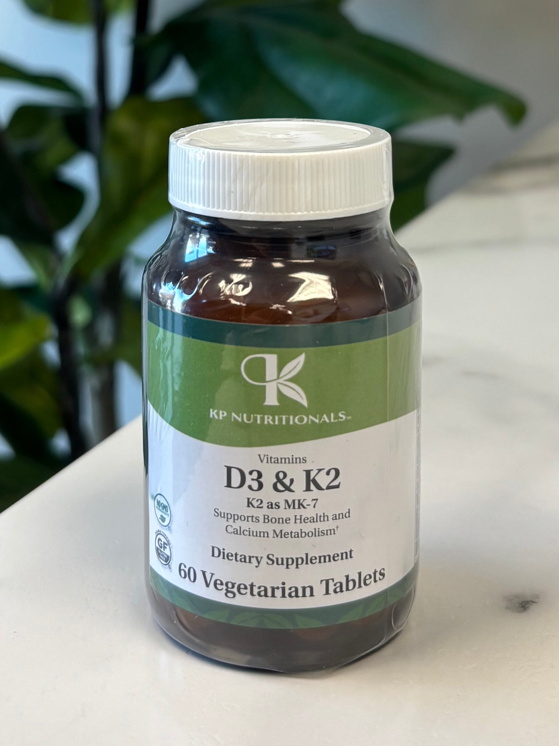 Bottle of Vitamin D3 & K2 Supplement on a marble surface with green leaves in the foreground