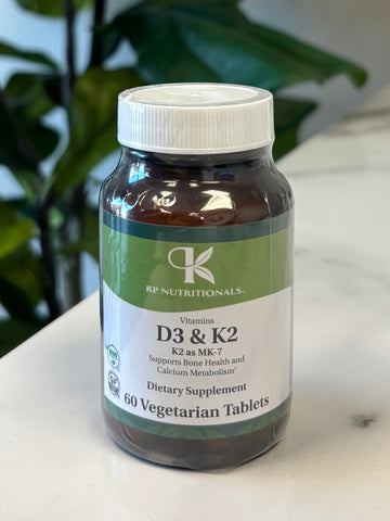 Bottle of Vitamin D3 & K2 Supplement on a marble surface with green leaves in the foreground